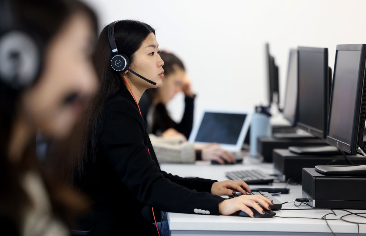 Student sat at desktop computers, wearing headsets.