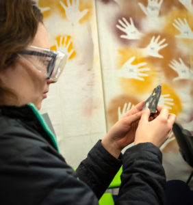 Female student examining a flint in front of a painting of hand prints